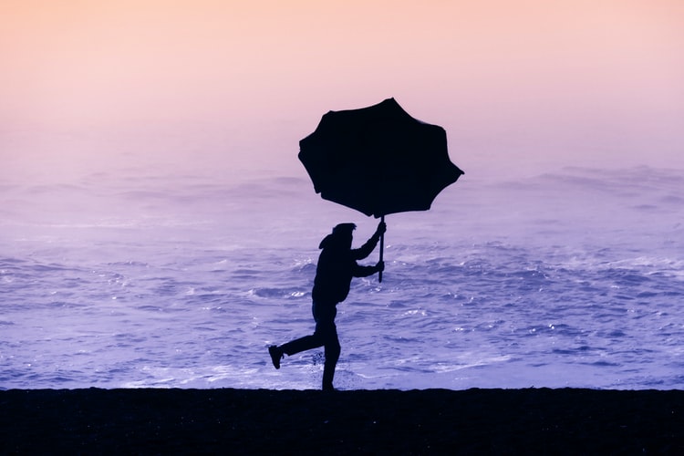 eine Person, die aufgrund des starken Windes den Schirm festhält Strandschirm Foto