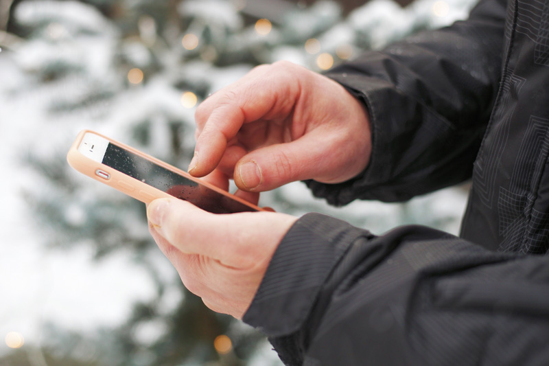 Ein Mann verwendet ein Handy mit Gummihülle draußen und im Winter Akku schonen: Verwende eine Handyhülle oder ein Handy-Etui im Winter