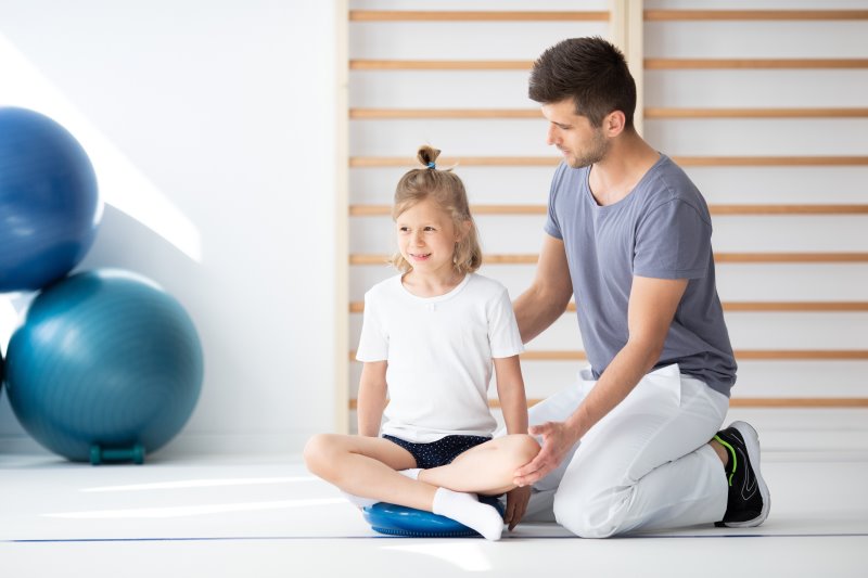 Mädchen auf Balancekissen erhält Anweisung von einem Pysiotherapeuten Balancekissen in der Physiotherapie