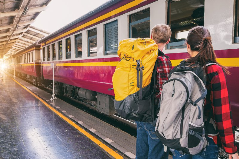 Zwei Menschen am Gleis mit Reiserucksäcken die auf den Einfahrenden Zug warten Festival Packen mit Rucksack