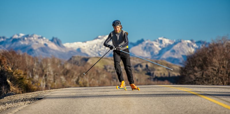 Skiroller-Läufer im Skating-Stil mit Schutzausrüstung vor einer Berglandschaft