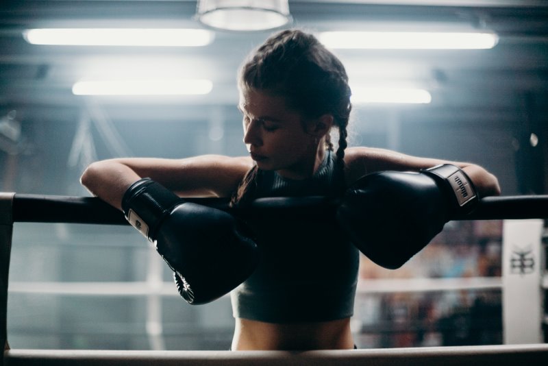 Eine Frau mit Boxhandschuhen lehnt über der Absperrung eines Boxrings Standboxsack als Ergänzung zum Zweikampf