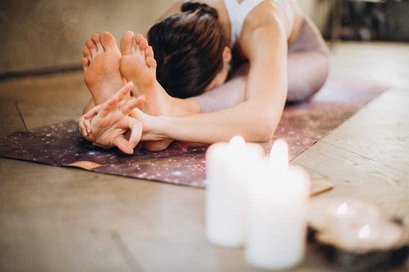 Frau, die auf einer Yogamatte entspanntes Yoga macht und Kerzen dabei an hat in entspannter Atmosphäre wird Yoga praktikziert