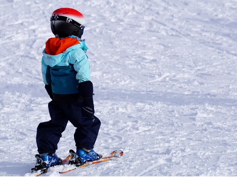 Kind steht mit Kinderskihelm auf der Piste Kind steht mit einem Kinderskihelm auf einer Skipiste