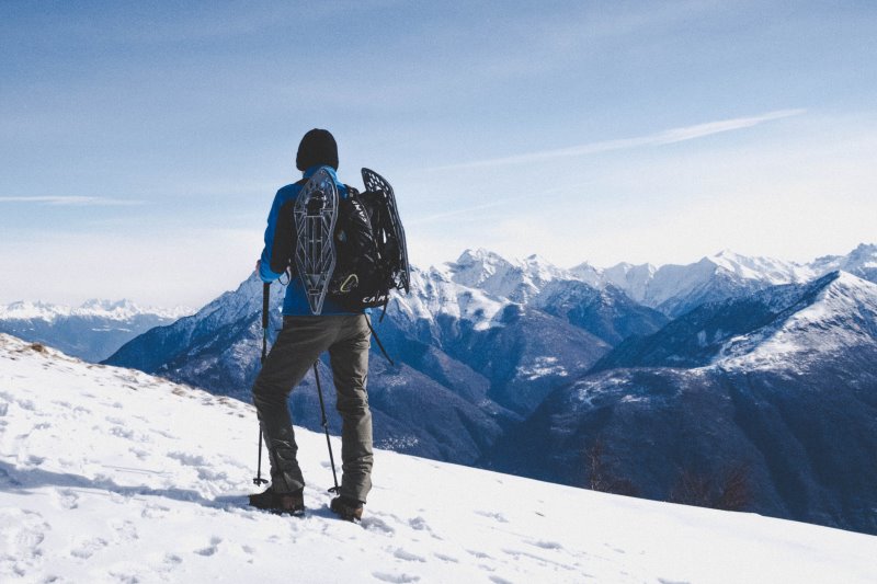 Mann steht im Schnee und sieht auf Berge Lawinenpiepser und LVS-Geraet mit Zubehoer