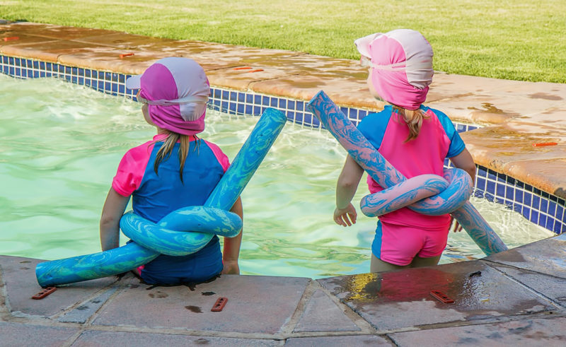 zwei kleine Mädchen stehen im Pool Zwei Kinder mit Schwimmnudel