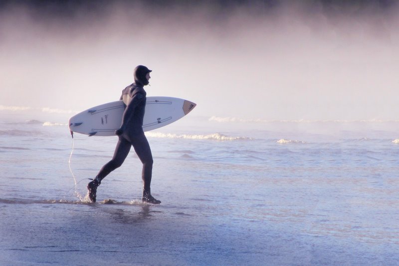 Surfer geht mit dickem Neoprenanzug & -schuhen surfen Surfer trägt Winter-Booties