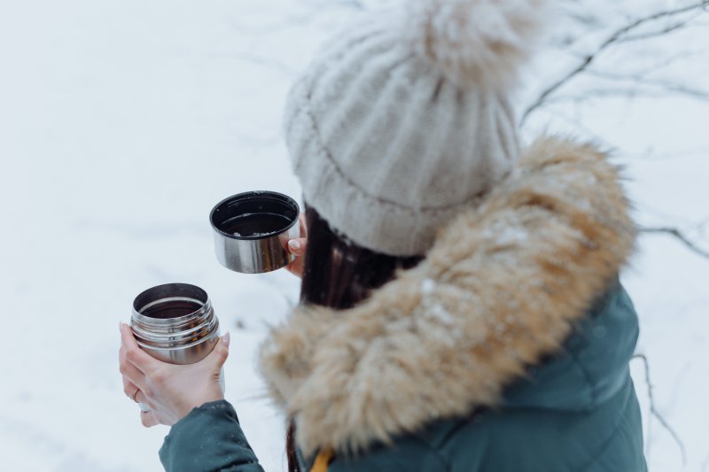 Thermoskanne im Test Frau ist im Schnee und trinkt aus ihrer Thermoskanne