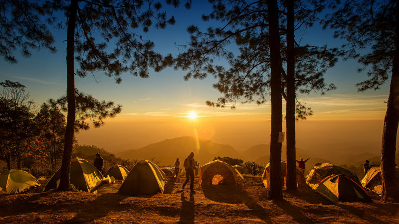 Viele Trekkingzelte und Menschen mit Blick auf den Sonnenuntergang Trekkingzelte und Menschen bei Sonnenuntergang