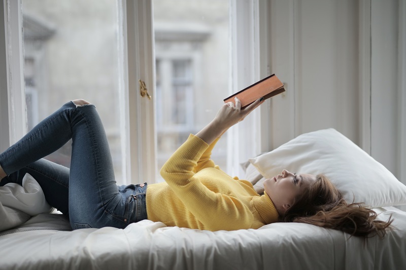 Die Leseposition Frau liest liegend ein Buch auf dem Bett