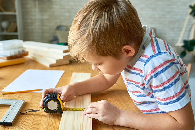 Im Werkunterricht mit Holz und Werkzeugen arbeiten Junge misst Holz ab