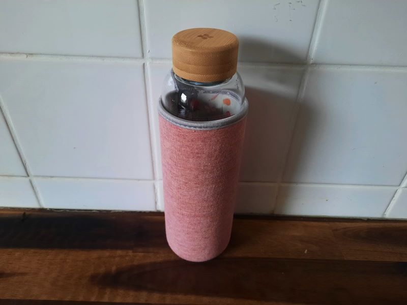 Elegante Glasflasche mit Bambusdeckel Glasflasche mit rosa Schutzhülle auf einer Holzoberfläche