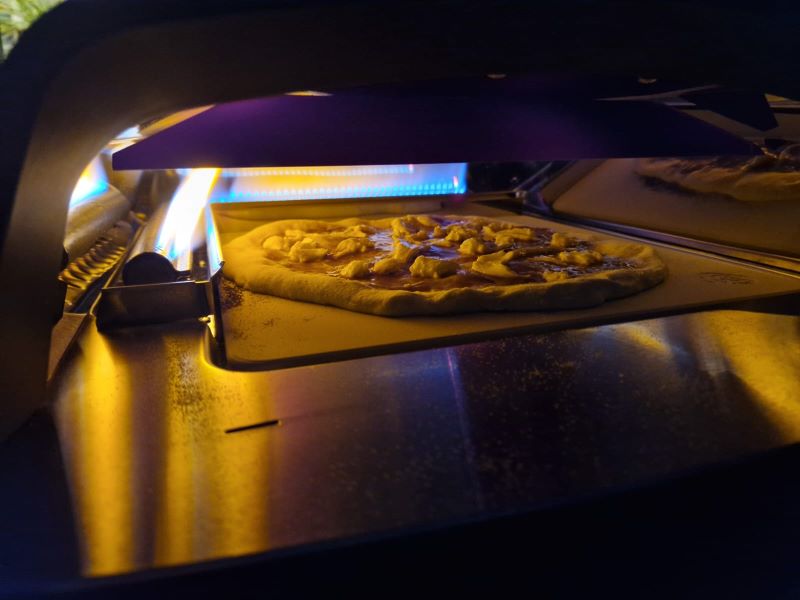 Pizza beim Backvorgang mit aktiviertem Brenner im Pizzaofen.