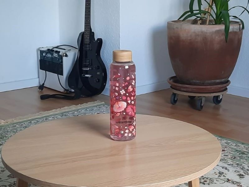 Stilvolle Waterdrop-Flasche in modernem Wohnambiente Eine mit Blumen bedruckte Waterdrop-Flasche auf einem runden Holztisch